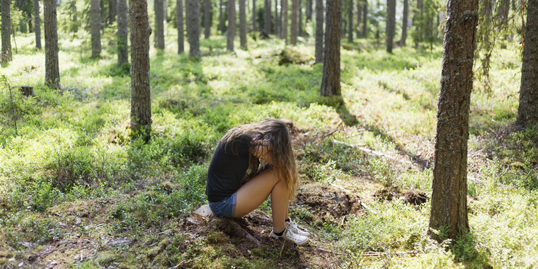 En flicka sitter i skogen med huvudet framåtlutat.
