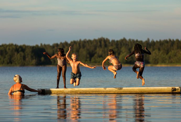 barn hoppar i vattnet från brygga i sjö i kvällsljus