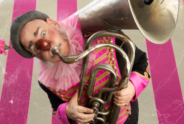 Clown spelar trombon framför cirkus