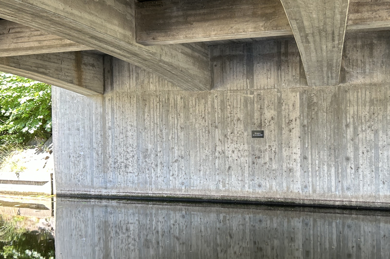 Skylt på betongvägg under bron
