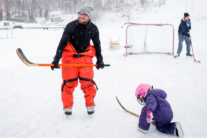 Pappa och dotter spelar hockey på is utomhus i vintrigt landskap.