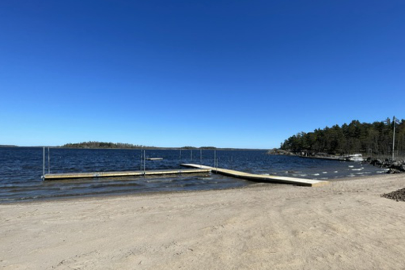 Badplatsen Uddhamn i Herräng. En stor sandstrand med bryggor. 